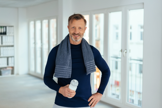 Father’s Day Male Vitality – Regenerative Performance Care A fit, confident middle-aged man smiling with a gym towel and water bottle, representing male vitality and regenerative longevity treatments.